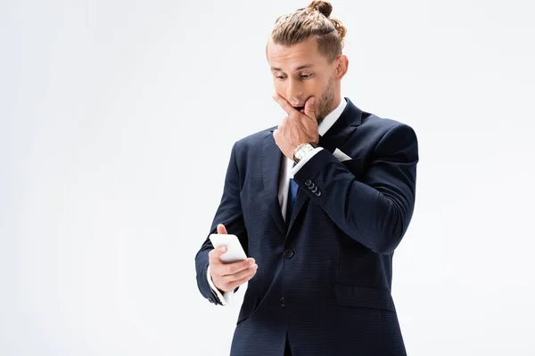 Confuso joven hombre de negocios en traje con teléfono inteligente aislado en blanco - foto de stock