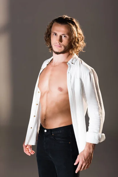 Homme sexy avec chemise déboutonnée posant sur fond sombre — Photo de stock