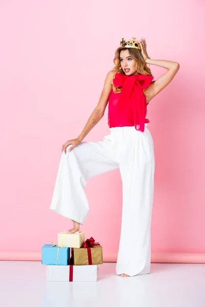 Mulher elegante na coroa com presentes no fundo rosa — Fotografia de Stock