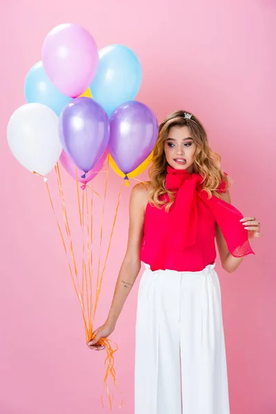 Elegante mujer confundida en corona con globos sobre fondo rosa - foto de stock