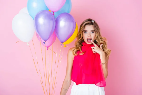 Elegante mujer sorprendida en corona con globos sobre fondo rosa - foto de stock