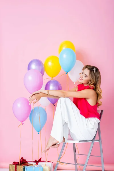 Elegante mujer feliz en corona con globos sobre fondo rosa - foto de stock