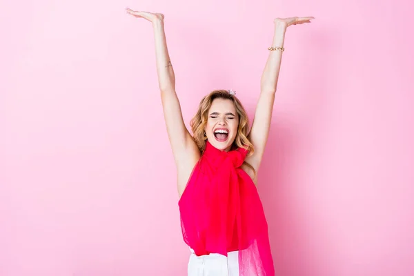 Elegante mujer feliz en la corona con las manos levantadas sobre fondo rosa - foto de stock
