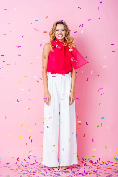 Élégante femme heureuse en couronne sous confettis sur fond rose — Photo de stock