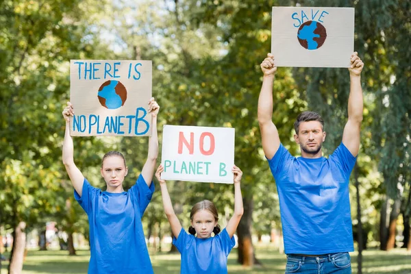 Familia de voluntarios sosteniendo pancartas con el globo terráqueo, excepto, y sin inscripción planeta b en manos levantadas, concepto de ecología - foto de stock