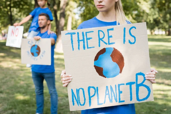 Mulher segurando cartaz com globo e não há nenhuma inscrição planeta b perto da família com cartazes em fundo borrado, conceito de ecologia — Fotografia de Stock