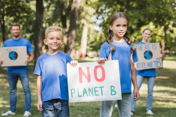 Niños sosteniendo pancarta sin inscripción planeta b cerca de padres con carteles sobre fondo borroso, concepto de ecología - foto de stock