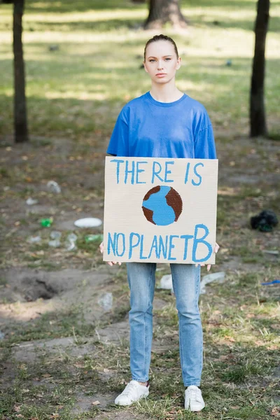 Woman looking at camera while holding placard with globe and there is no planet b inscription — Stock Photo