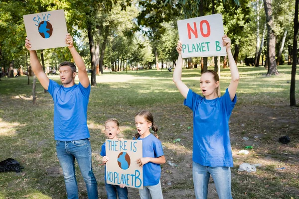 Familia de voluntarios gritando mientras sostienen pancartas con el globo y sin inscripción planeta b, concepto de ecología - foto de stock