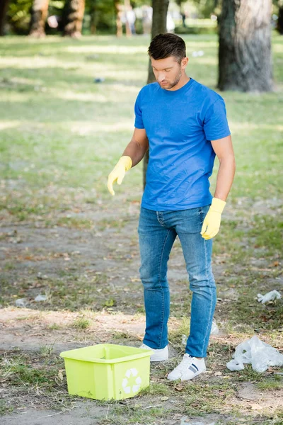 Man in rubber gloves standing near container with recycling sign — Stock Photo