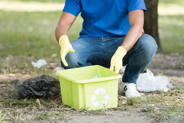 Vista parcial del hombre recogiendo residuos plásticos en contenedor con emblema de reciclaje - foto de stock