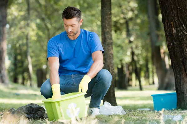Homem coleta de lixo plástico em recipiente, foreground borrado — Fotografia de Stock
