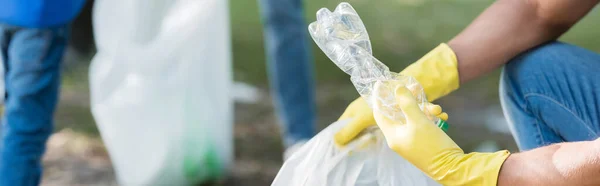 Обрізаний вид людини в гумових рукавичках, що тримає пластикову пляшку поблизу сім'ї на розмитому тлі, концепція екології, банер — стокове фото