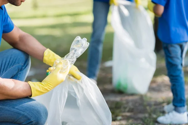 Abgeschnittene Ansicht eines Mannes mit Plastikflasche und recycelter Tasche in der Nähe einer Familie auf verschwommenem Hintergrund, Ökologiekonzept — Stockfoto