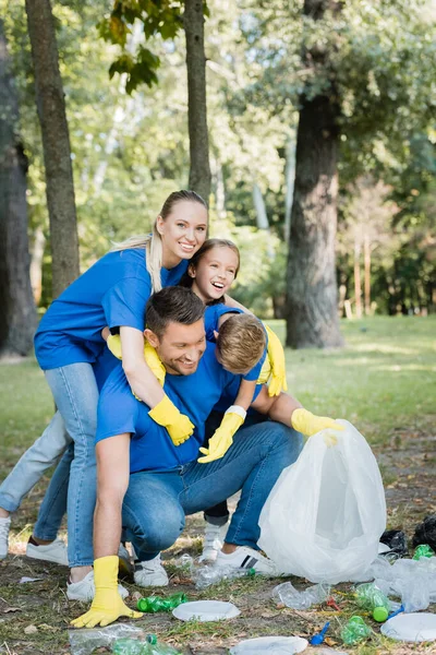 Familia feliz abrazo padre mientras recoge basura de plástico en el bosque, concepto de ecología - foto de stock