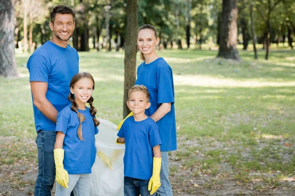 Familia feliz de activistas mirando a la cámara mientras están de pie con bolsa reciclada en el bosque, concepto de ecología - foto de stock