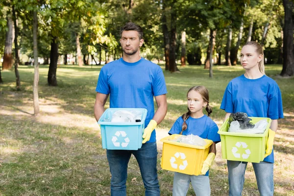 Familia de voluntarios sosteniendo contenedores con carteles de reciclaje, llenos de basura plástica, concepto de ecología - foto de stock