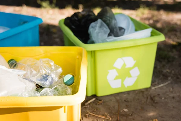 Contenitori con emblemi di riciclaggio, pieni di rifiuti plastici su fondo sfocato, concetto di ecologia — Foto stock