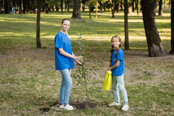 Happy mother and daughter planting young tree in forest, ecology concept — Stock Photo