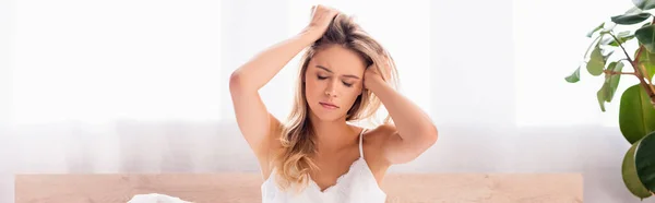 Young woman with hands near head suffering from headache in bedroom, banner — Stock Photo