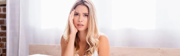 Confused woman with hand near cheek looking at camera at home, banner — Stock Photo