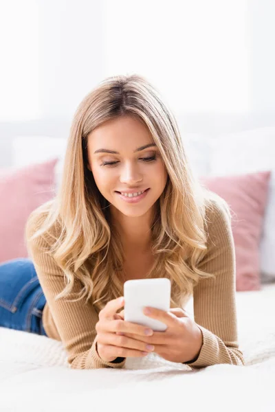 Mulher positiva usando smartphone enquanto deitada na cama — Fotografia de Stock