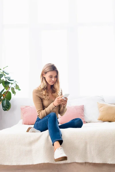 Mujer joven en ropa casual usando teléfono inteligente en la cama — Stock Photo