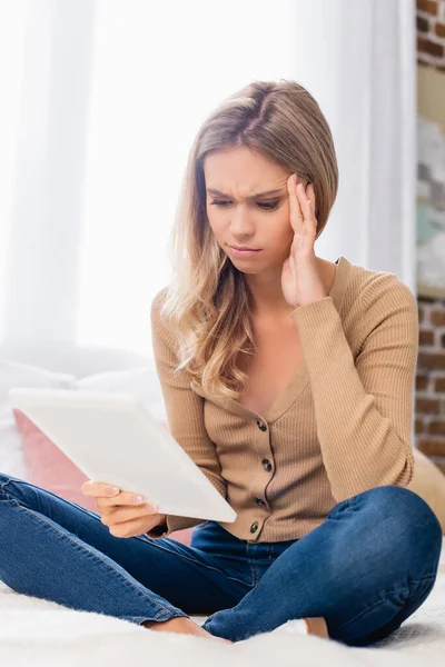 Pensive woman with hand near head using digital tablet on bed — Stock Photo