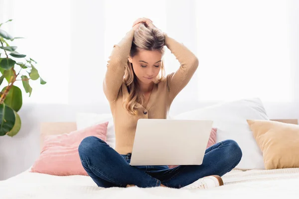 Joven freelancer con las manos cerca de la cabeza usando portátil en la cama - foto de stock