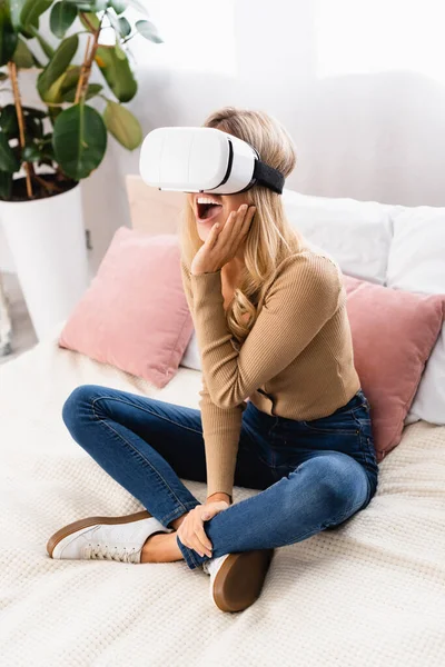 Excited woman in vr headset sitting on bed at home — Stock Photo