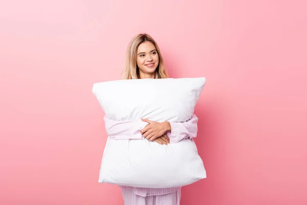 Mujer sonriente en pijama sosteniendo almohada blanca sobre fondo rosa - foto de stock