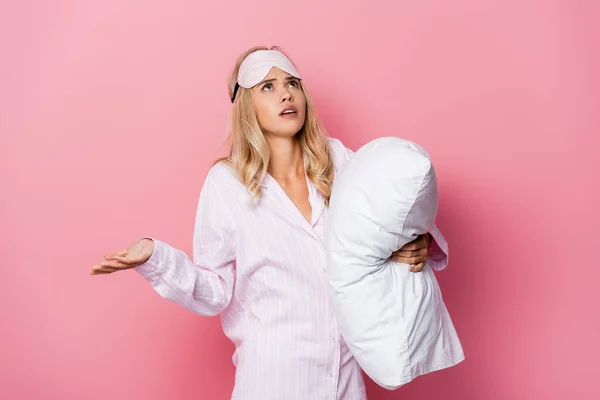 Confused woman in pajamas looking up and holding pillow on pink background — Stock Photo