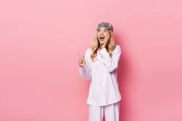 Mujer excitada con los ojos vendados y pijamas señalando con el dedo el fondo rosa - foto de stock