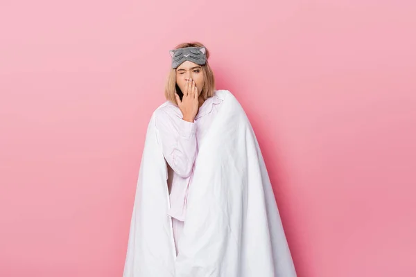 Mujer somnolienta en pijama y manta bostezando sobre fondo rosa - foto de stock