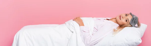 Молодая женщина в пижаме лежит на подушке с одеялом на розовом фоне, баннер — стоковое фото