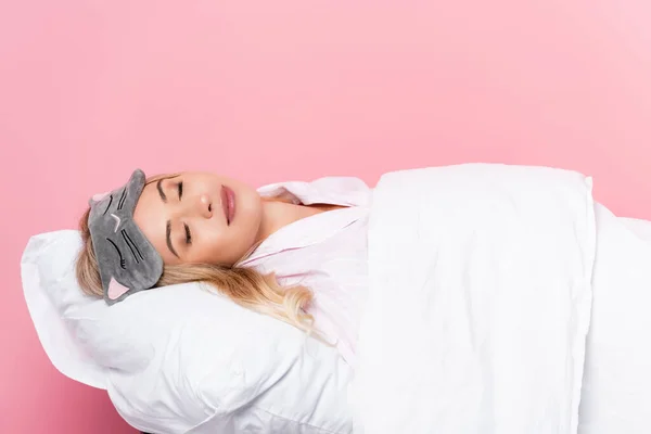 Mujer joven con los ojos vendados durmiendo en la almohada con manta sobre fondo rosa - foto de stock