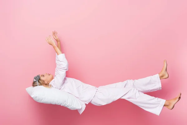 Mujer joven en pijama acostada sobre almohada sobre fondo rosa - foto de stock