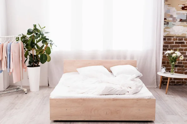 Dormitorio con plantas, despertador y perchero con ropa - foto de stock