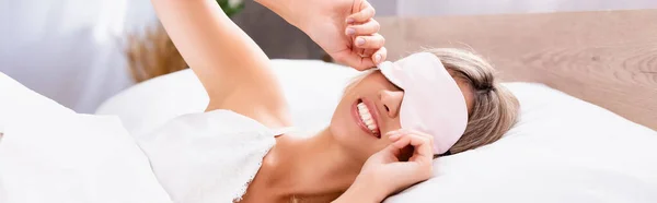 Femme souriante en pyjama portant les yeux bandés sur le lit le matin, bannière — Photo de stock