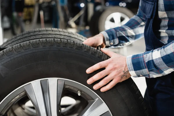 Cropped view of technician moving car wheel in workshop — Stock Photo