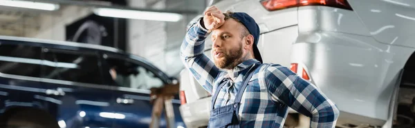 Giovane riparatore stanco che si tiene per mano vicino alla fronte in officina, banner — Foto stock