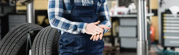 Vue partielle du réparateur frottant les mains tout en se tenant près des roues de la voiture dans le garage — Photo de stock