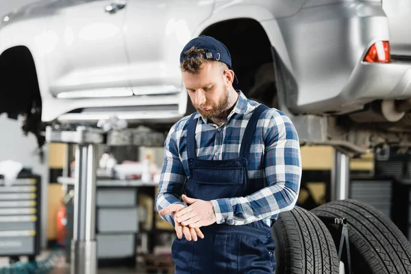 Technician rubbing hands near auto raised on car lift on blurred background — Stock Photo