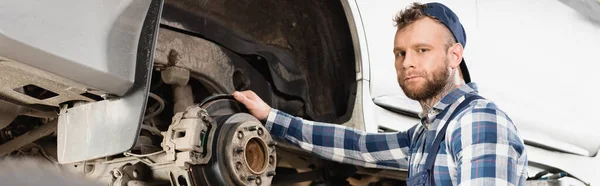 Young technician looking at camera while holding hand on brake disk, banner — Stock Photo