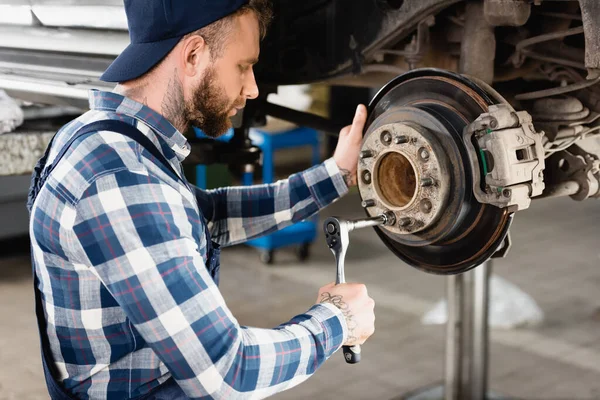 Mechanic fixing wheel hub with wrench on automobile, raised on car lift — Stock Photo
