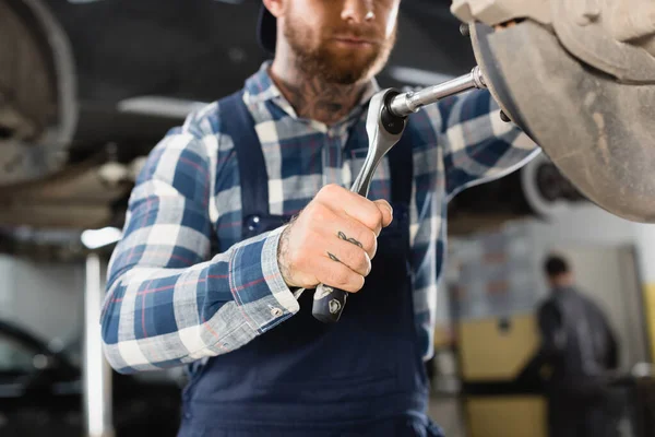 Cropped view of technician adjusting wheel hub with wrench on blurred background — Stock Photo