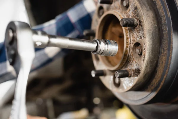 Nahaufnahme von Radnabe und Schraubenschlüssel in den Händen des Mechanikers auf verschwommenem Hintergrund — Stockfoto