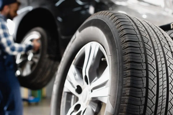 Vue rapprochée de la roue de la voiture près du technicien qui maintient la voiture sur fond flou — Photo de stock