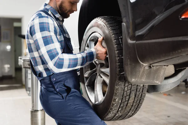 Vue recadrée de jeune technicien roue de fixation sur la voiture en atelier — Photo de stock