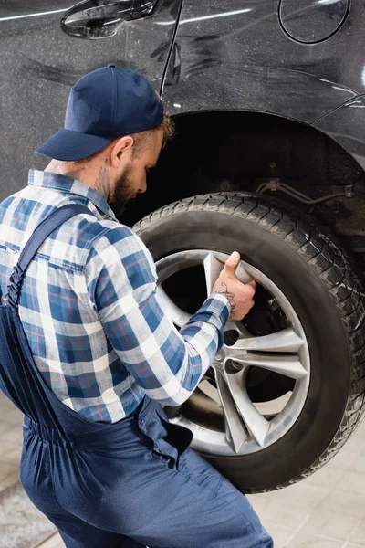 Vista posteriore del riparatore nella ruota di fissaggio dell'abbigliamento da lavoro sull'auto — Foto stock